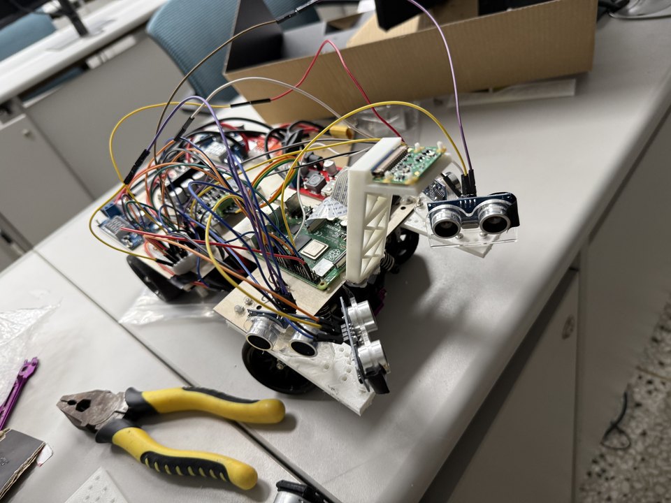 The self-driving car on a bench: a Raspberry Pi, motor drivers and ultrasonic sensors wired onto a flat chassis, pliers beside it.