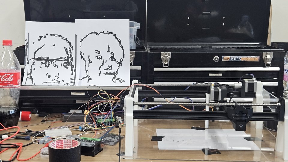 The pen plotter on a workbench with two finished line portraits standing up behind it.