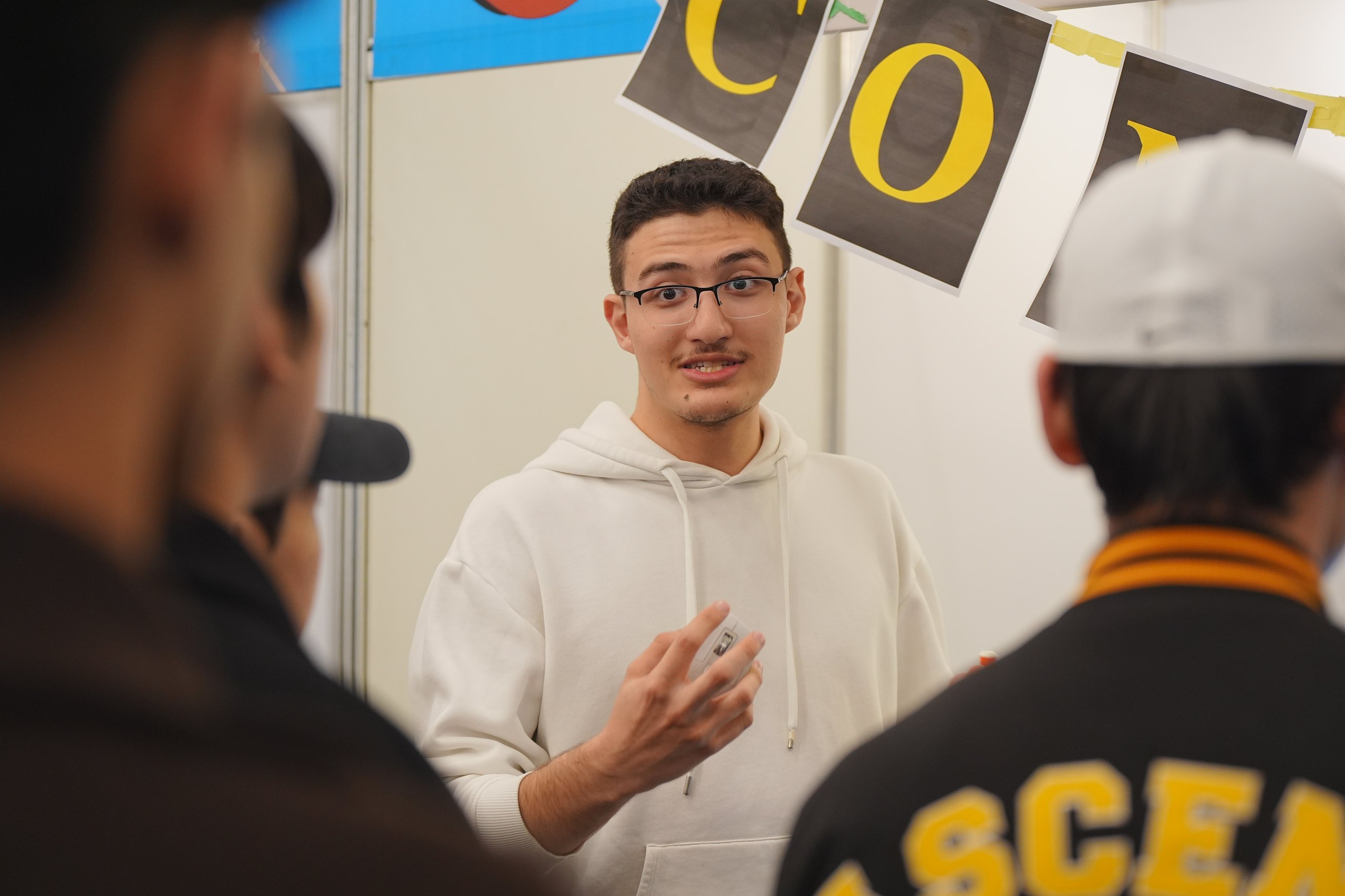 Abdullah mid-sentence with a microphone at an exhibition booth, hands moving as he explains something.