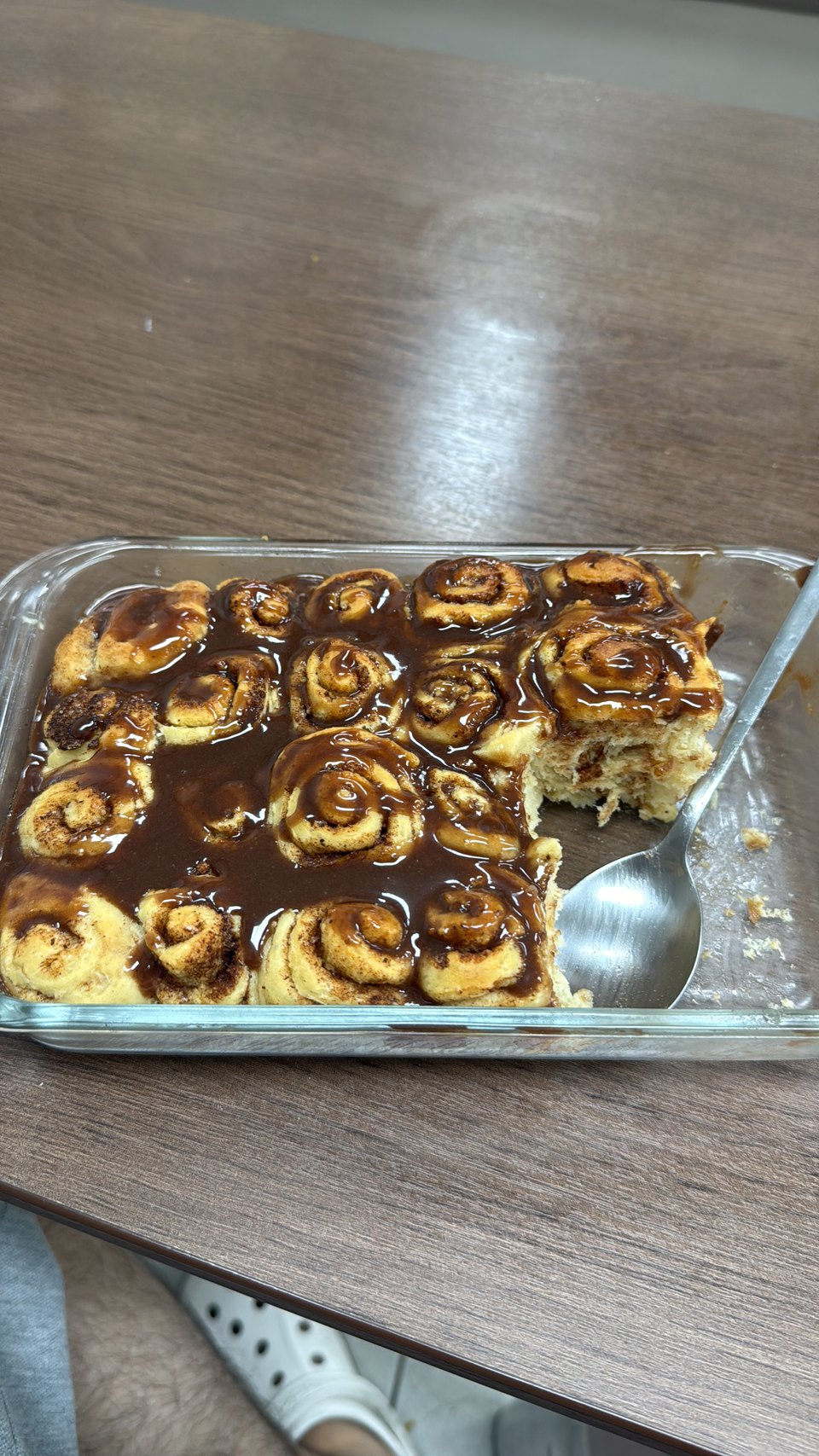 A tray of homemade cinnamon rolls under caramel sauce, one already lifted out.