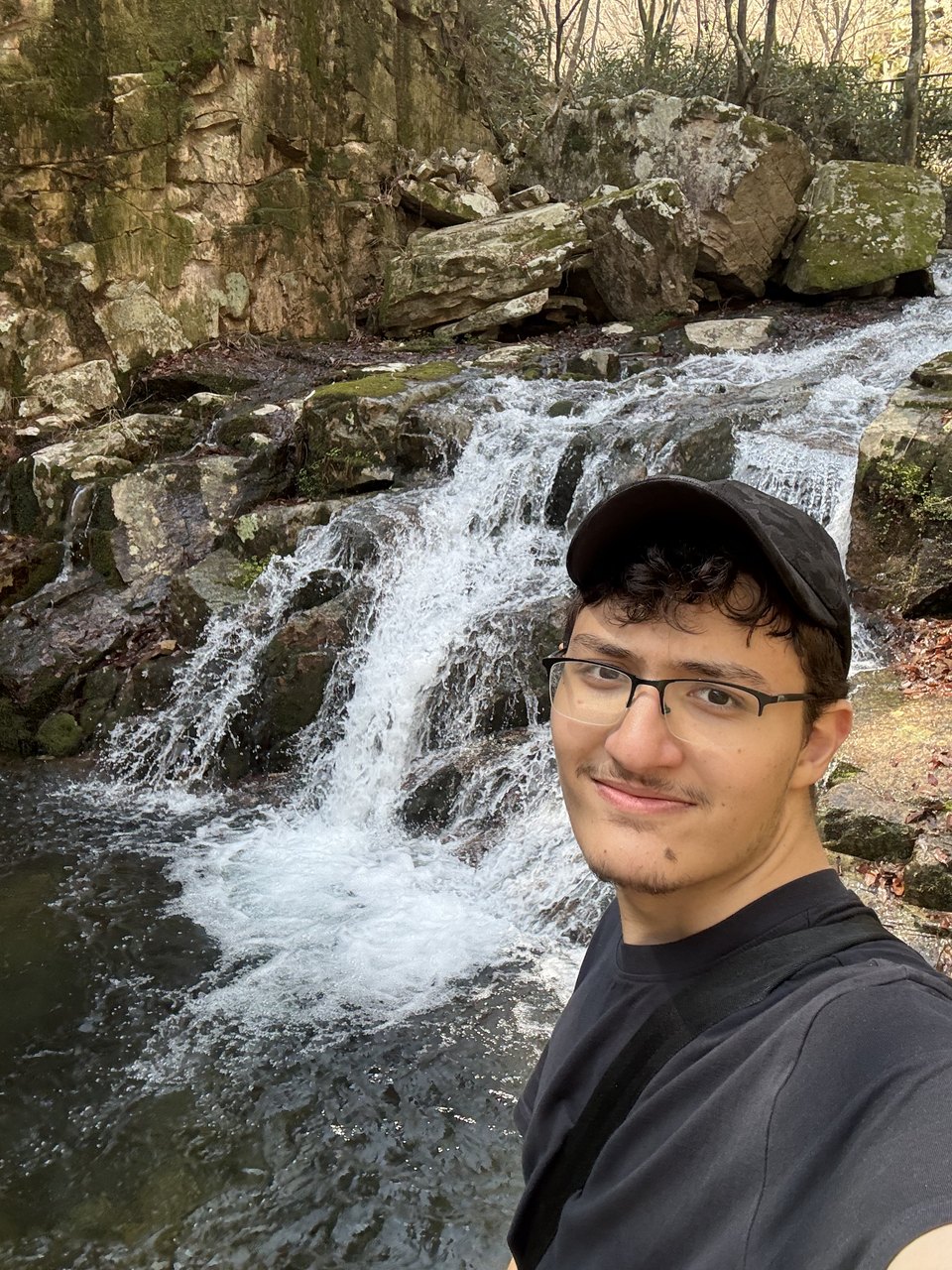 Abdullah in front of a waterfall on a rocky hillside.