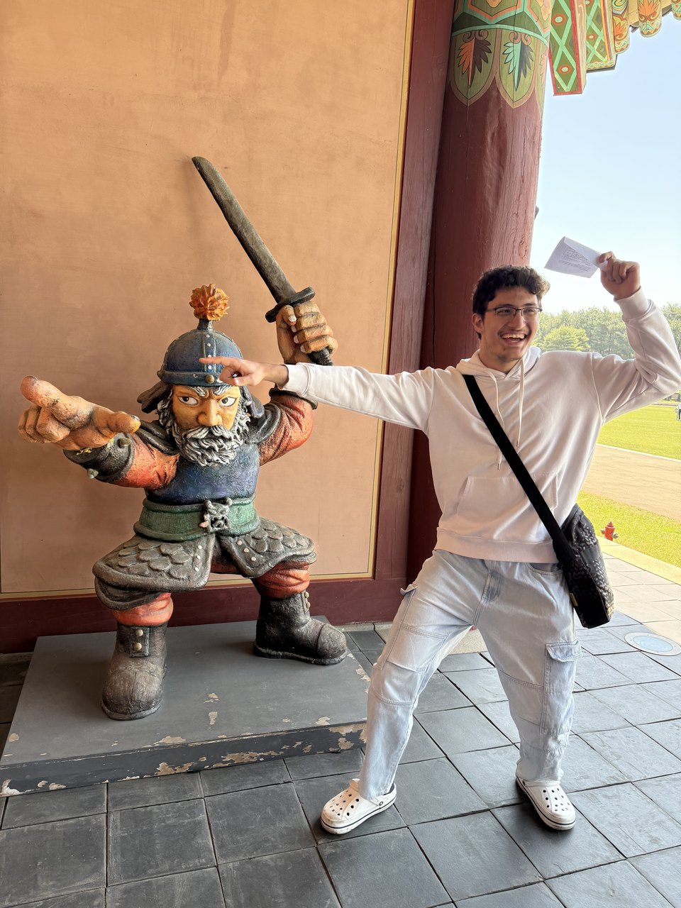 Abdullah copying the pose of a painted warrior statue at the gate of a Korean palace.