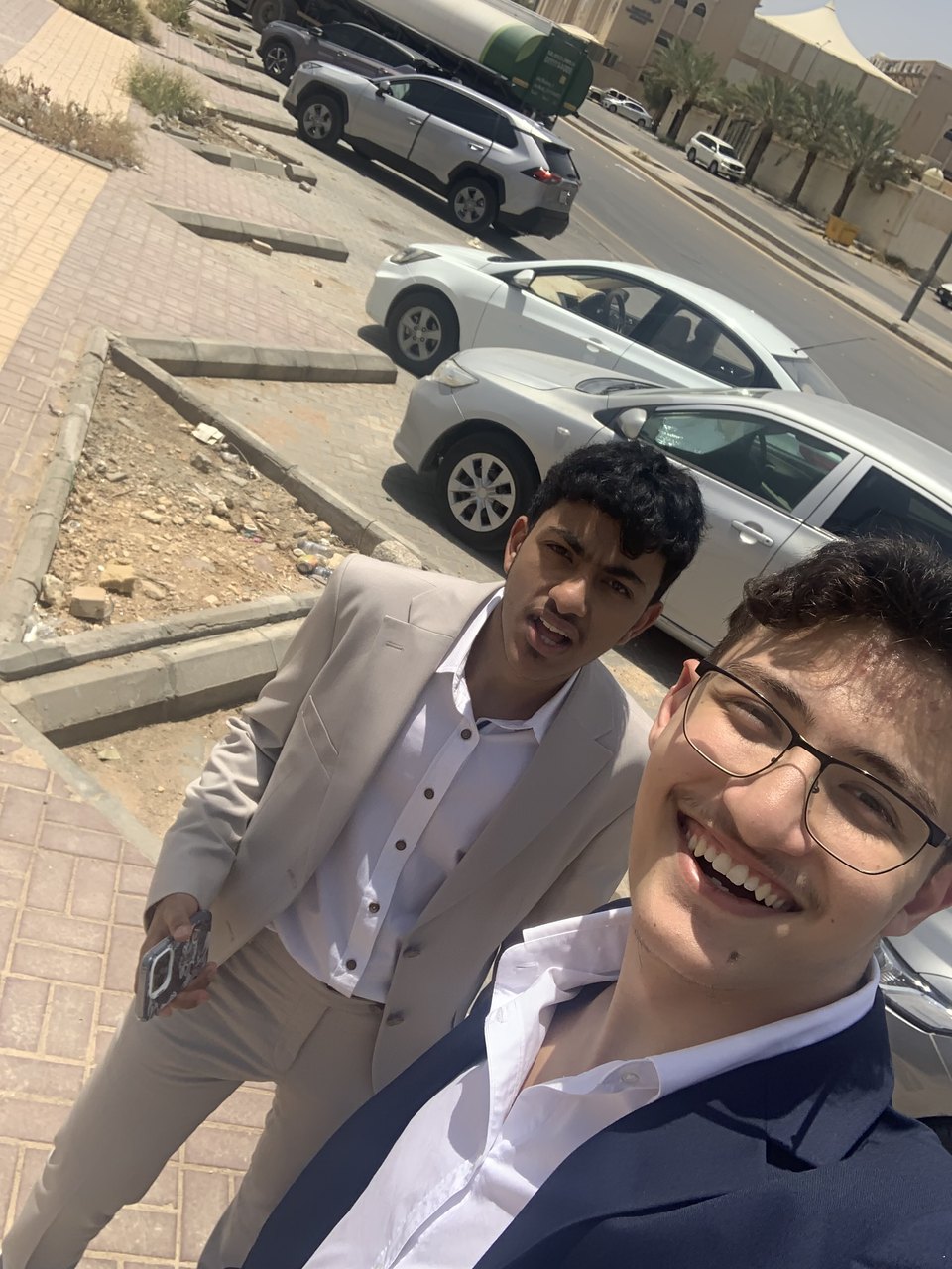 Abdullah and a friend in suits, taking a selfie on a sunlit street.