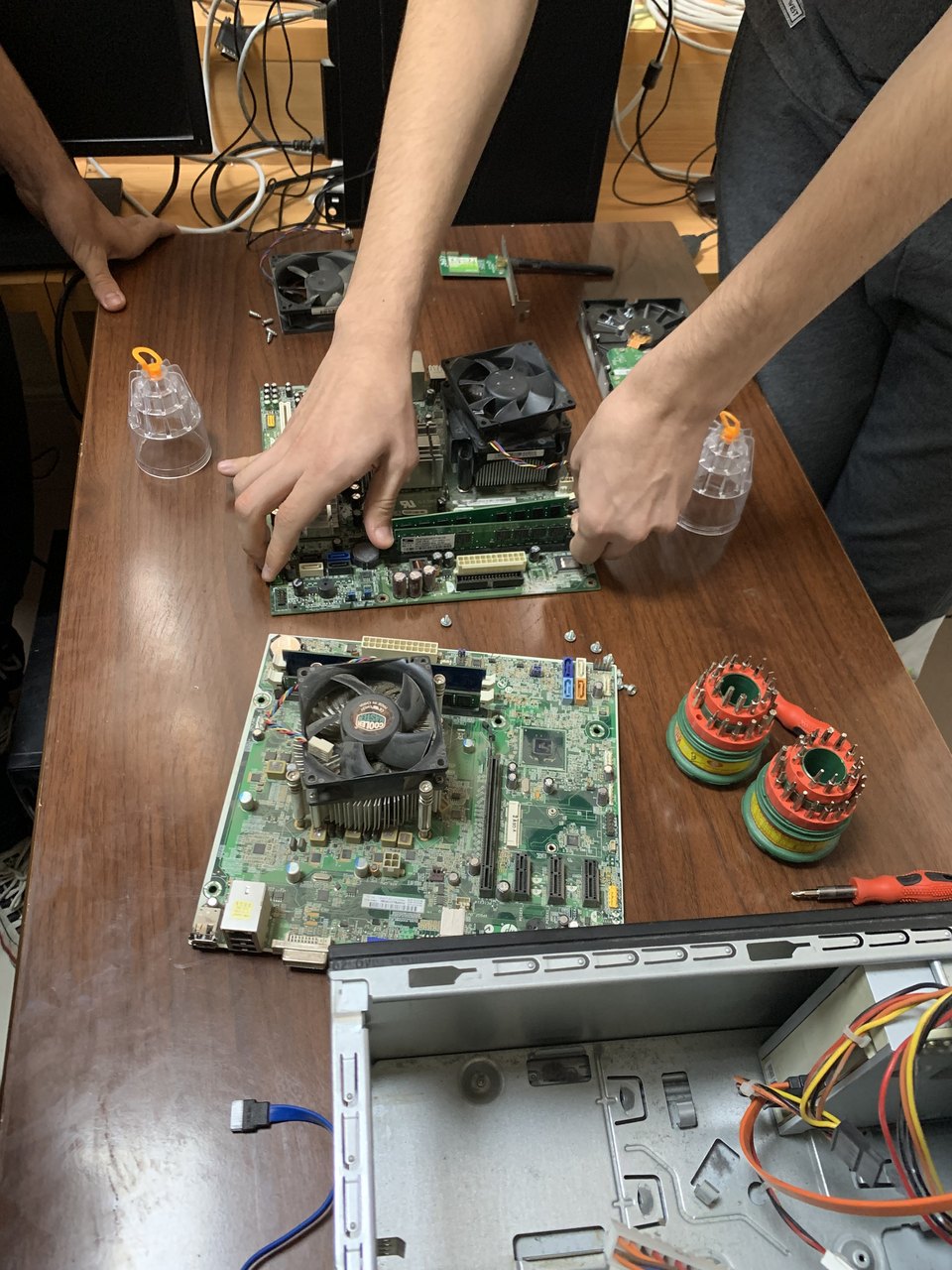 Hands reaching across a table covered in motherboards, CPU coolers and screwdrivers during a PC-building workshop.