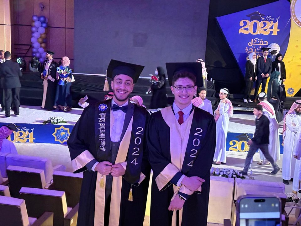 Abdullah and a classmate on stage in graduation robes, both wearing 2024 sashes.