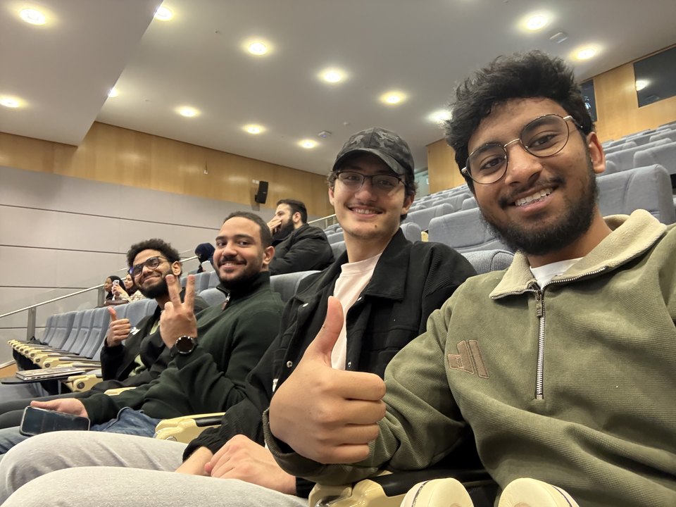 Abdullah and four friends in a lecture hall, thumbs up and peace signs at the camera.