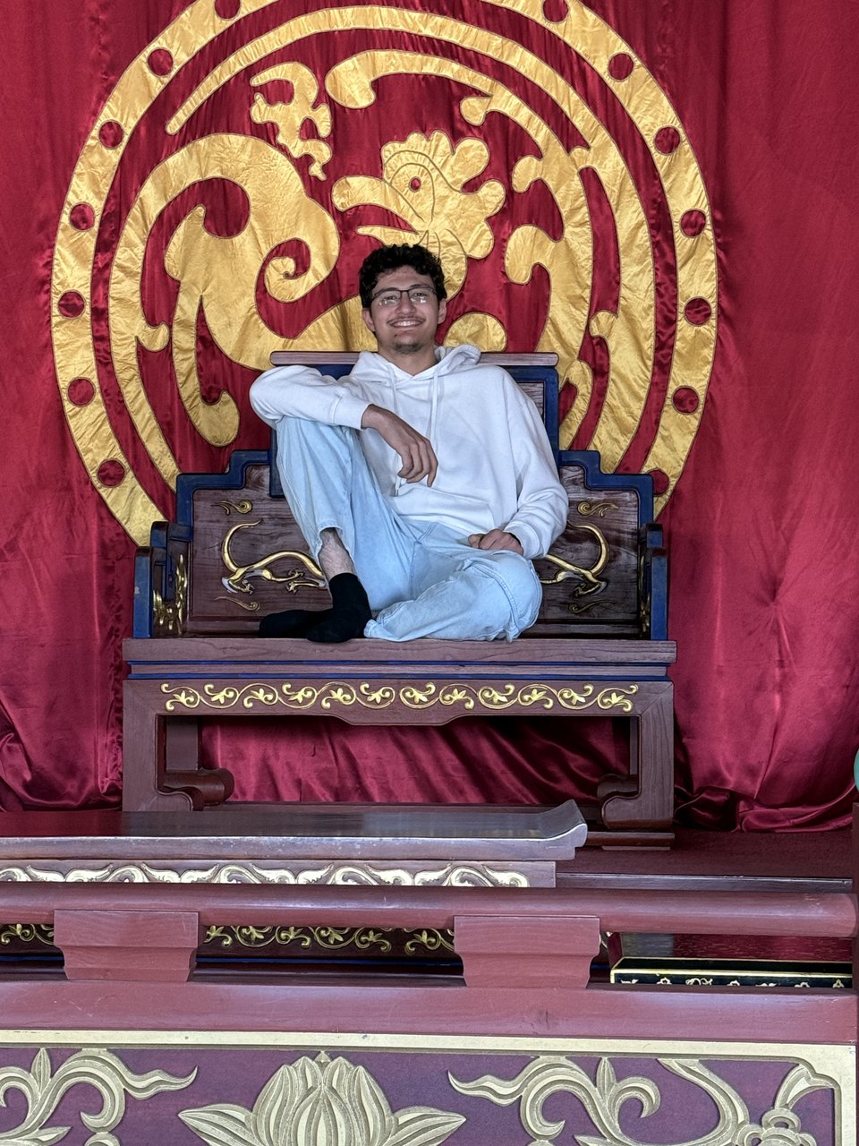 Abdullah sitting cross-legged on a Korean throne in front of a red and gold backdrop.
