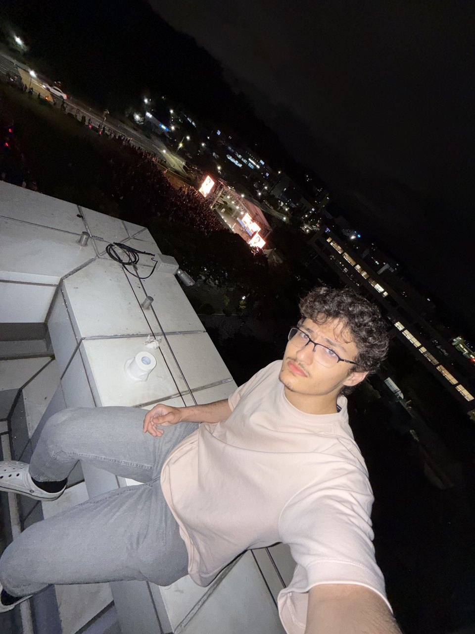 Abdullah leaning back against a railing at night with a lit city behind him.
