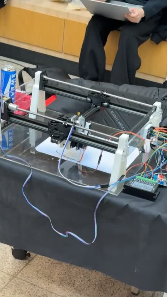 The pen plotter drawing a portrait, its gantry moving across the paper.